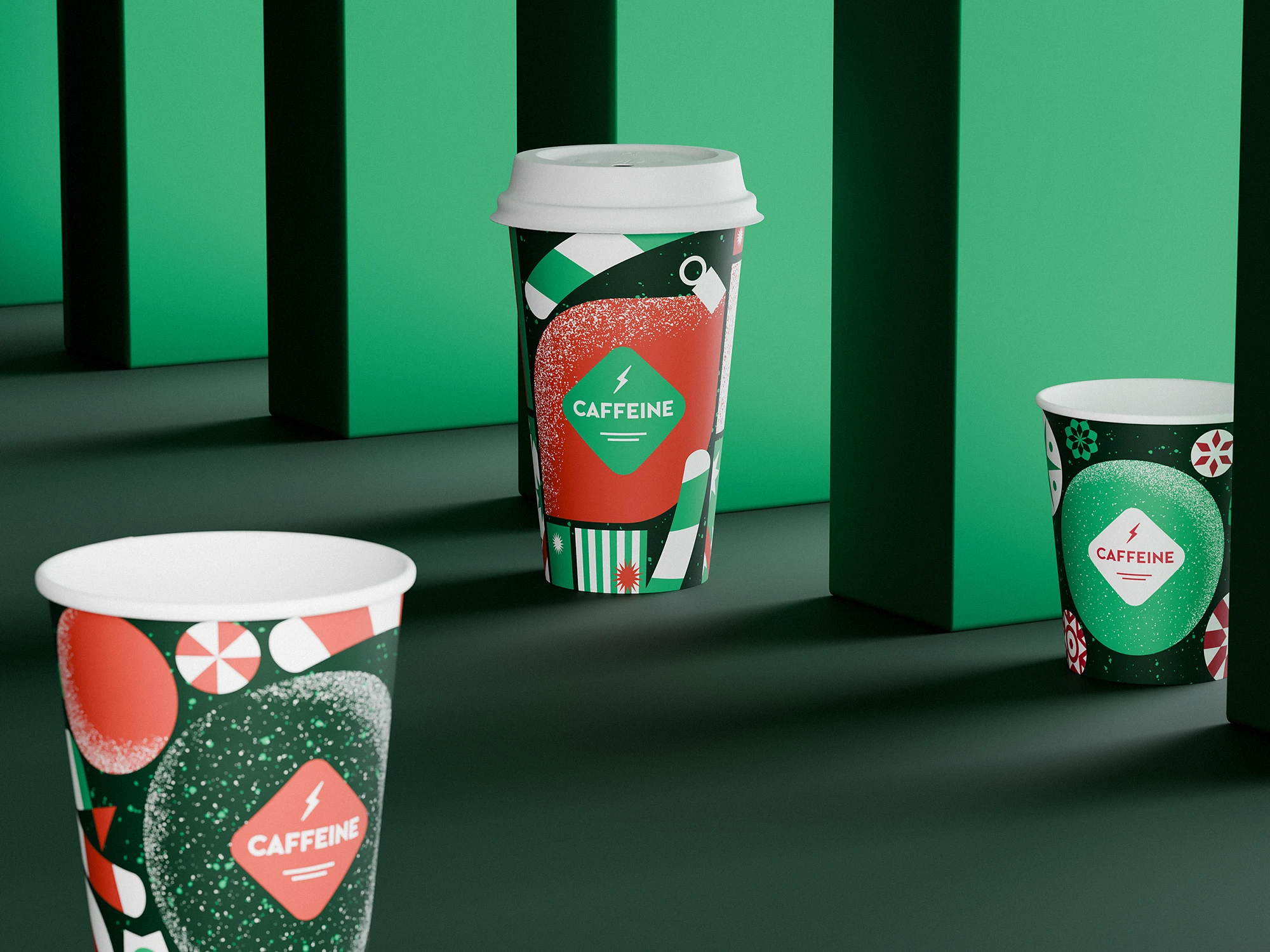 Three CAFFEINE Christmas edition cups (2023) displayed among tall green blocks. Each cup is decorated with festive patterns in red, green, and white, including candy shapes, stars, and snowy textures, with the CAFFEINE logo in a diamond frame.