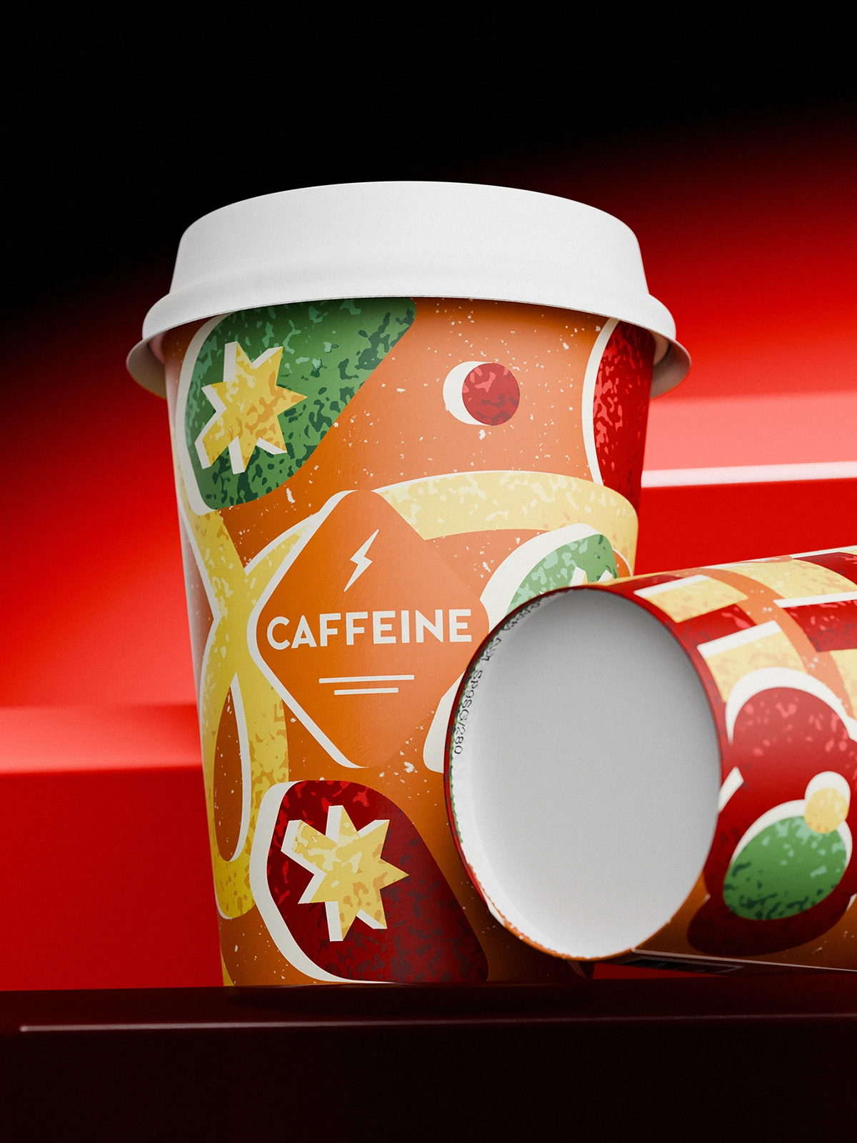 Close-up of CAFFEINE Christmas edition cup (2024) with white lid, standing on a red surface. The design features orange, green, red, and yellow festive illustrations — stars, baubles, ribbons, and abstract holiday shapes — with the CAFFEINE logo in a diamond frame at the center. Another cup lies sideways next to it.