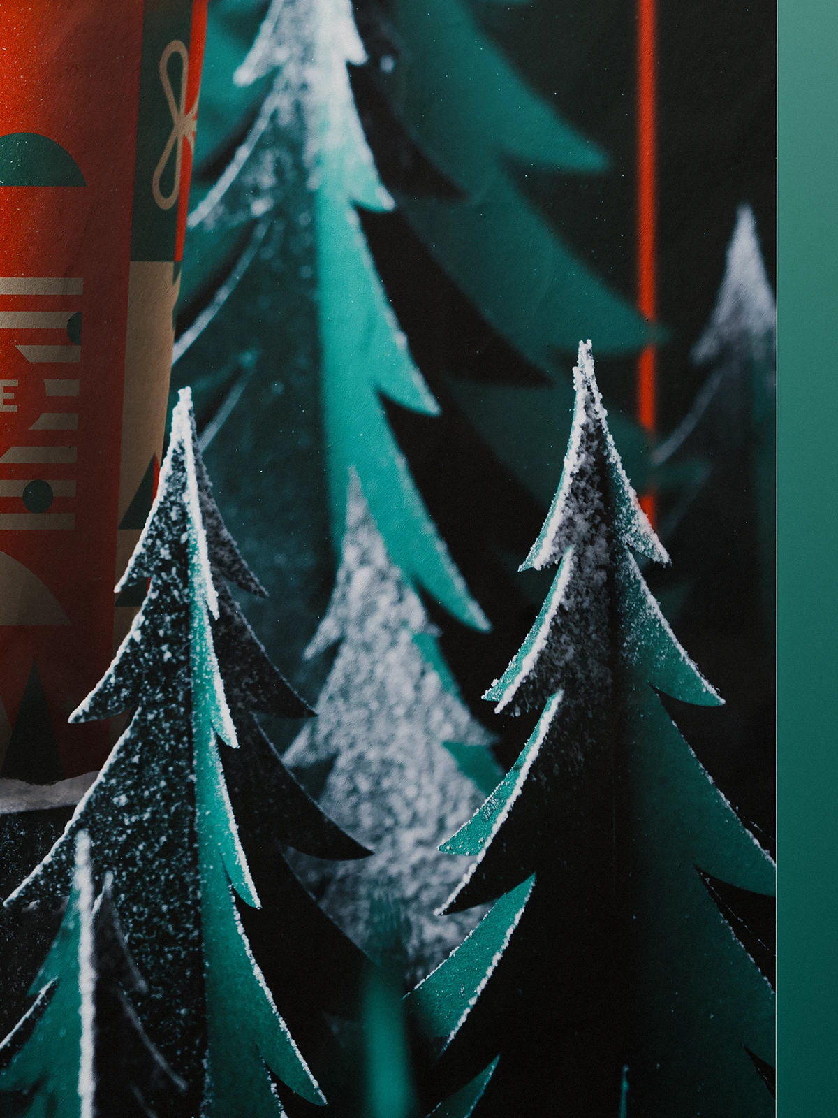 Close-up of paper-cut pine trees with snowy edges in front of a Christmas-themed Caffeine cup.