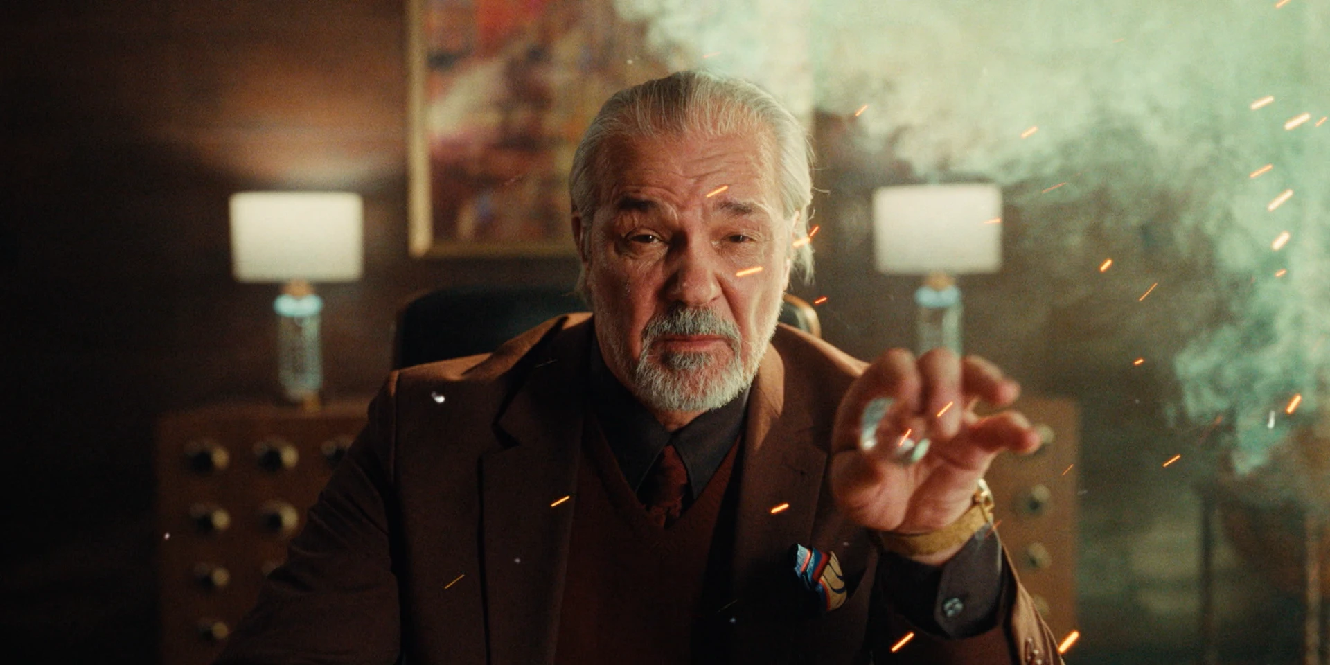 Close-up cinematic portrait of an older crime boss in a dark office interior, wearing a brown suit and holding a diamond between his fingers, with drifting smoke and glowing sparks in the air, warm dramatic lighting and shallow depth of field.